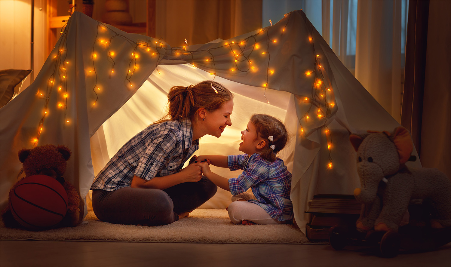 Mother and daughter in a homemade fort surrounded by fairy lights