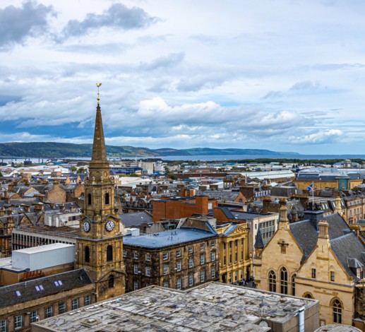 A view of the rooftops in Inverness on a still day, the sky is a mix of faint blues and whites, with hills visible in the distance. 