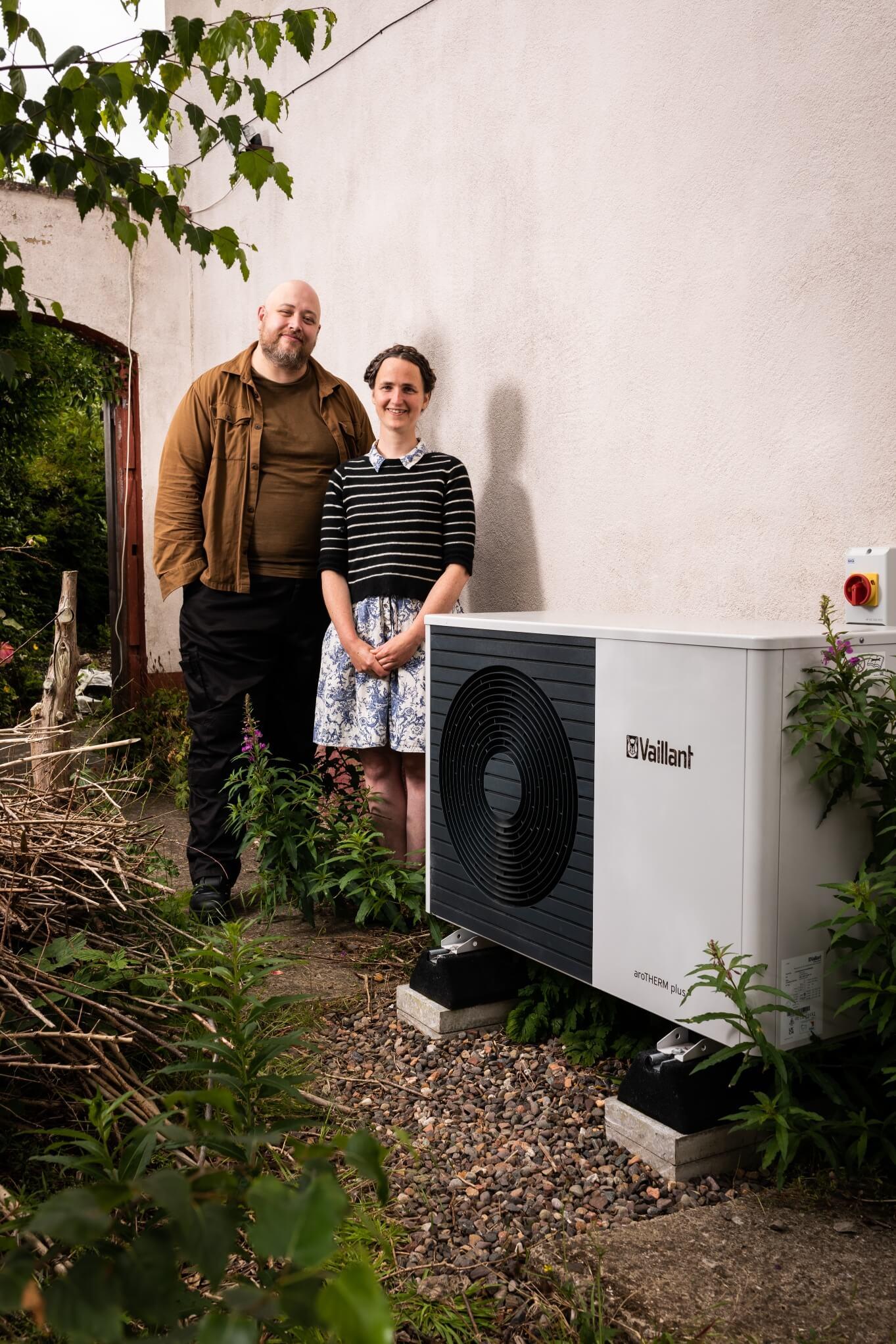 A man and a woman smiling and standing next to their heat pump outside their home