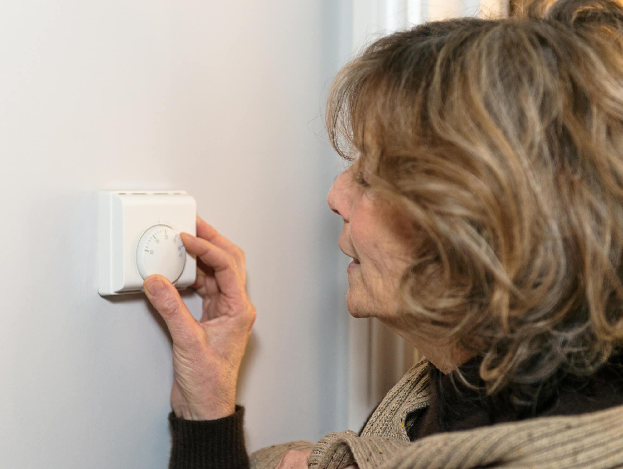 An older woman with short, light brown hair adjusts the heating controls in her house